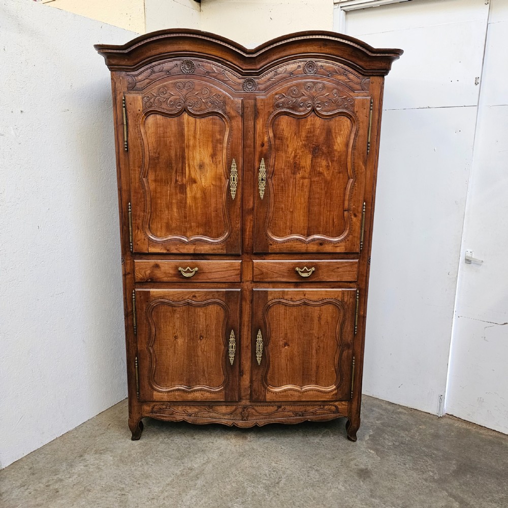 An 18th-century French carved walnut four-door armoire with shaped panels, central drawers, and decorative brass hardware.