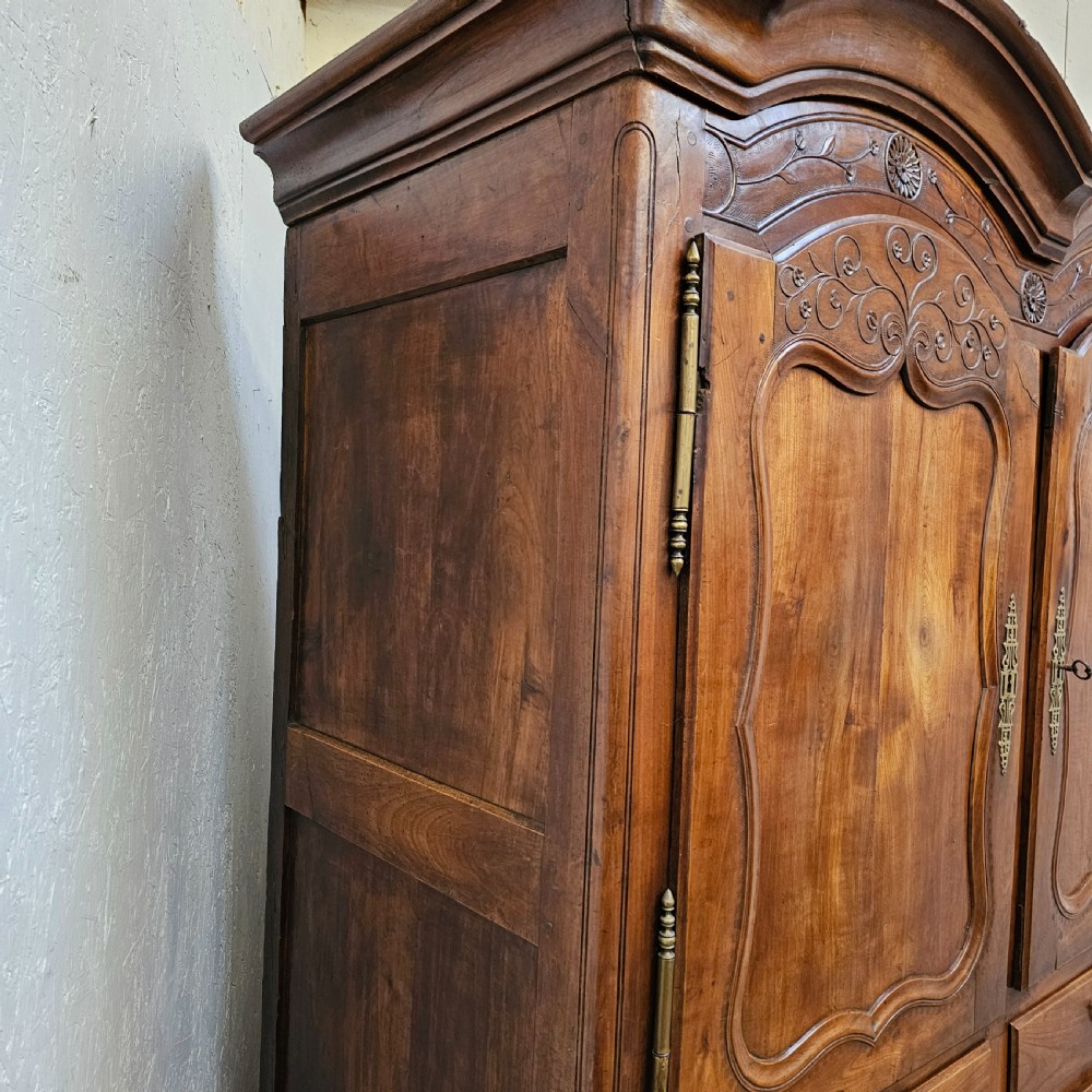An 18th-century French carved walnut four-door armoire with shaped panels, central drawers, and decorative brass hardware. View IV