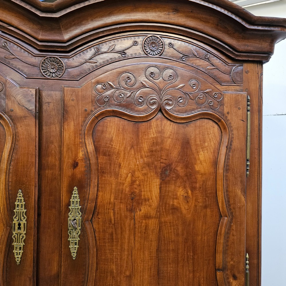 An 18th-century French carved walnut four-door armoire with shaped panels, central drawers, and decorative brass hardware. View V