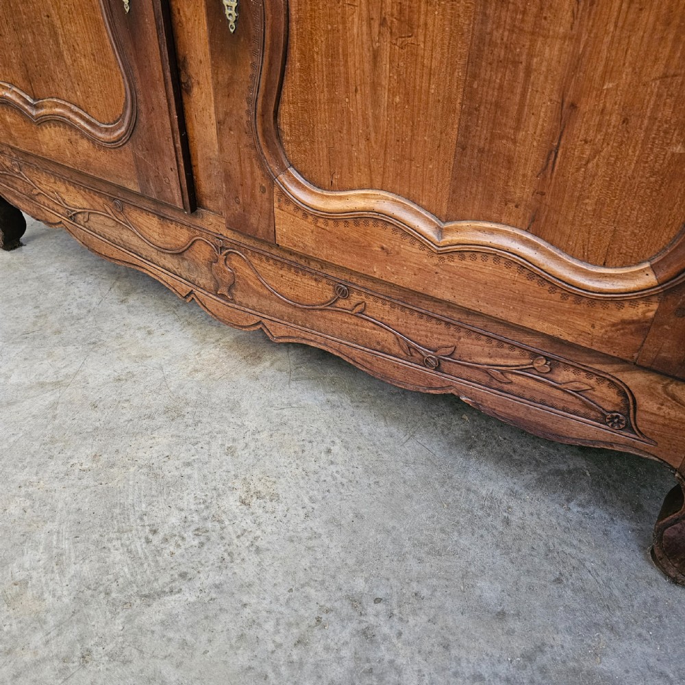 An 18th-century French carved walnut four-door armoire with shaped panels, central drawers, and decorative brass hardware. View VI