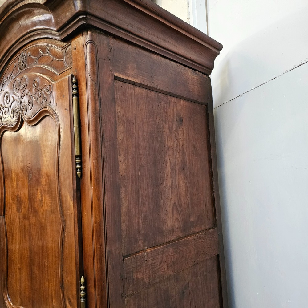 An 18th-century French carved walnut four-door armoire with shaped panels, central drawers, and decorative brass hardware. View VIII