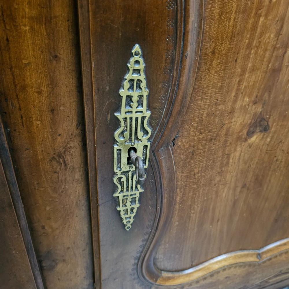 An 18th-century French carved walnut four-door armoire with shaped panels, central drawers, and decorative brass hardware. View IX