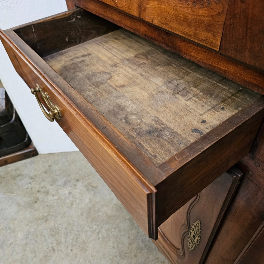 An 18th-century French carved walnut four-door armoire with shaped panels, central drawers, and decorative brass hardware. View X