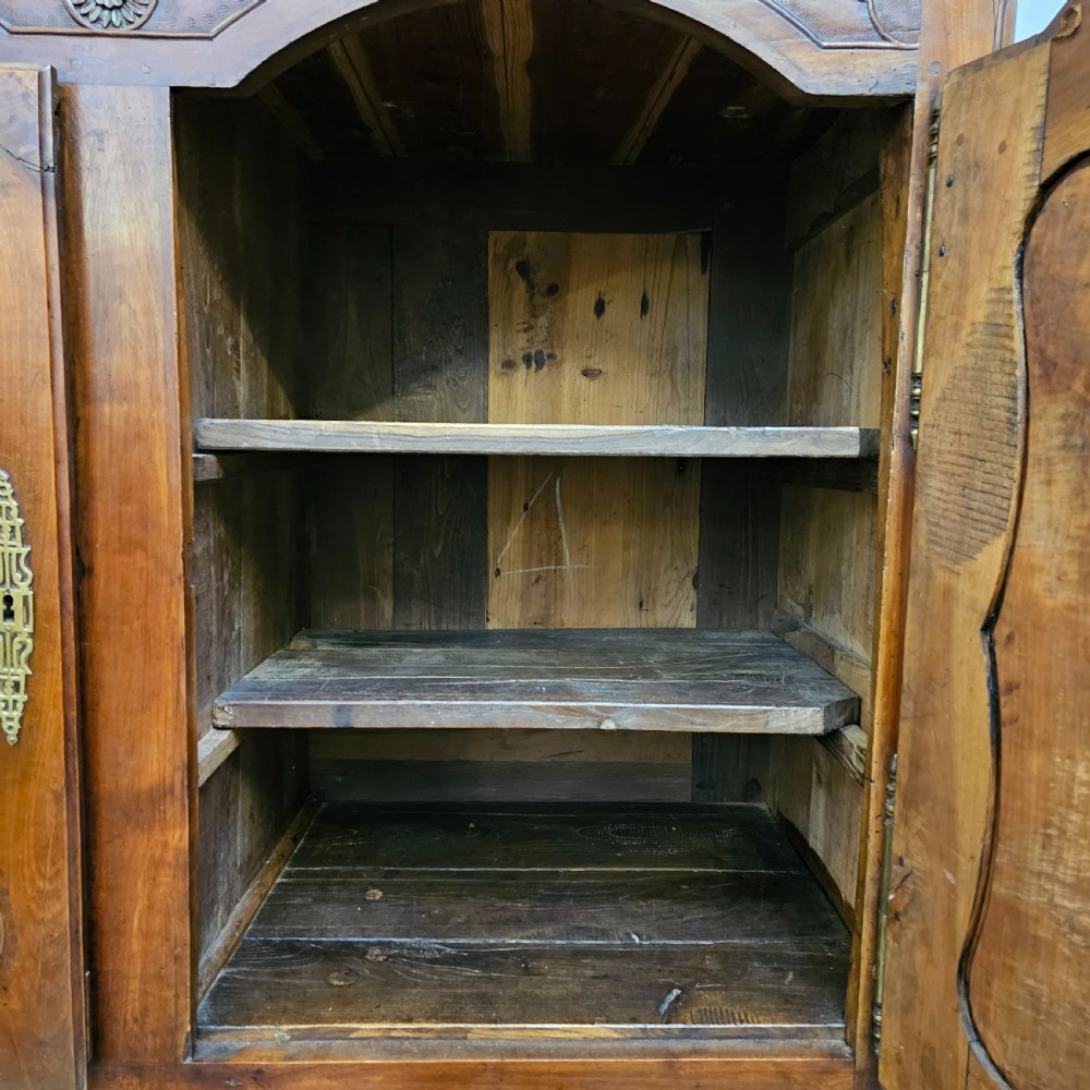 An 18th-century French carved walnut four-door armoire with shaped panels, central drawers, and decorative brass hardware. View XI