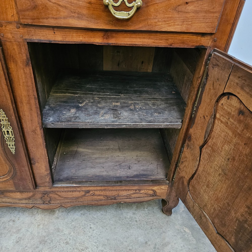 An 18th-century French carved walnut four-door armoire with shaped panels, central drawers, and decorative brass hardware. View XII