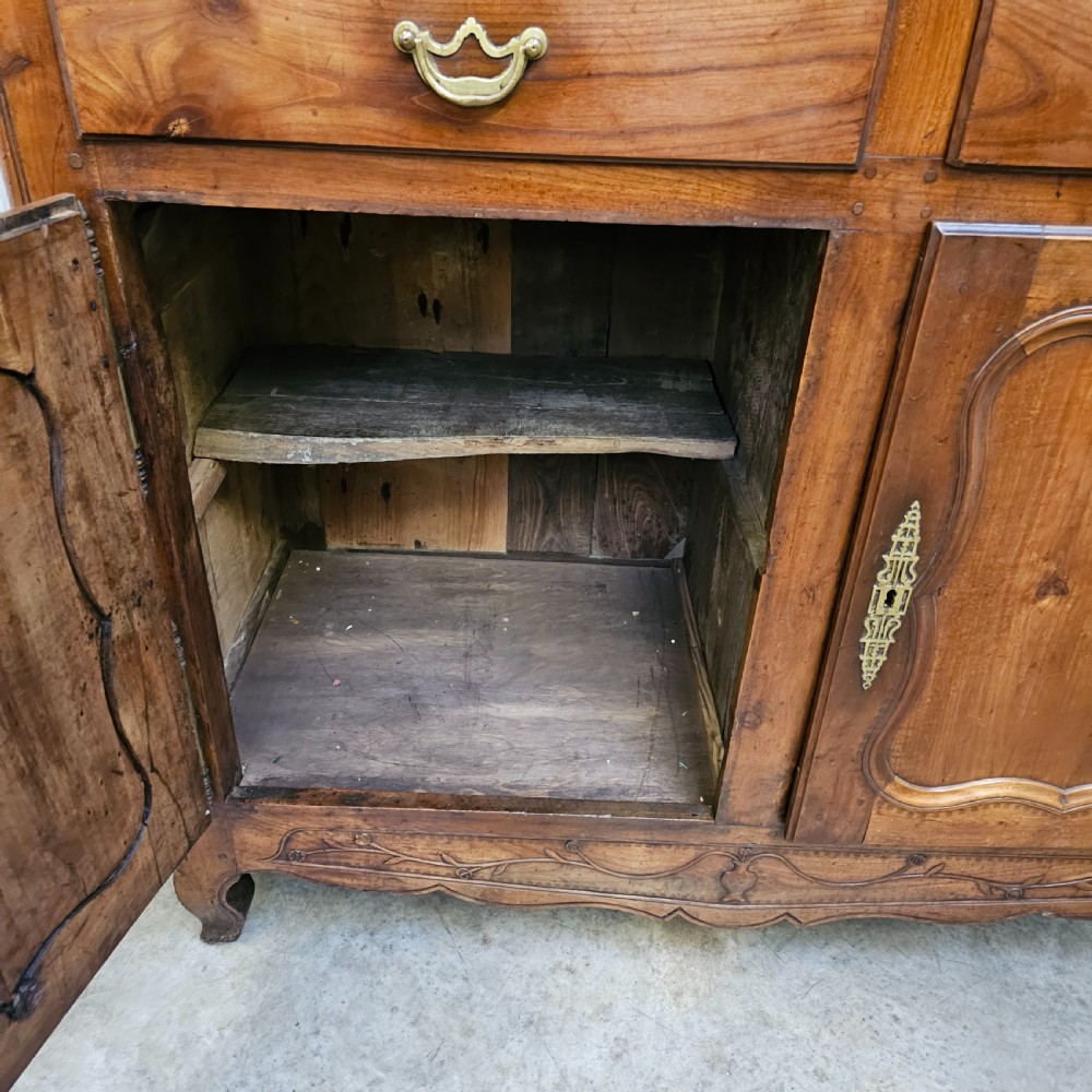 An 18th-century French carved walnut four-door armoire with shaped panels, central drawers, and decorative brass hardware. View XIII
