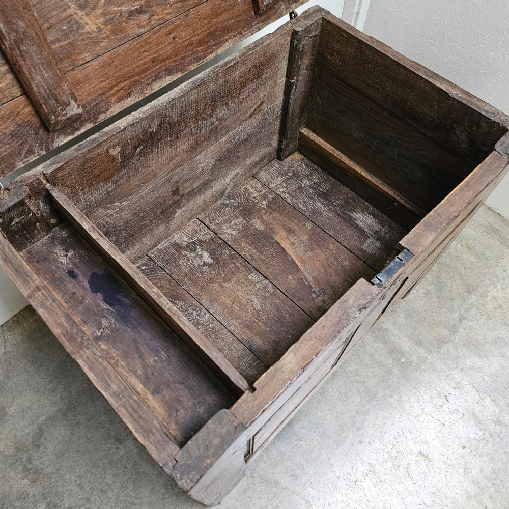 A solid dark oak coffer featuring a hinged rectangular top, two recessed front panels, and a central iron fleur-de-lis escutcheon. View V