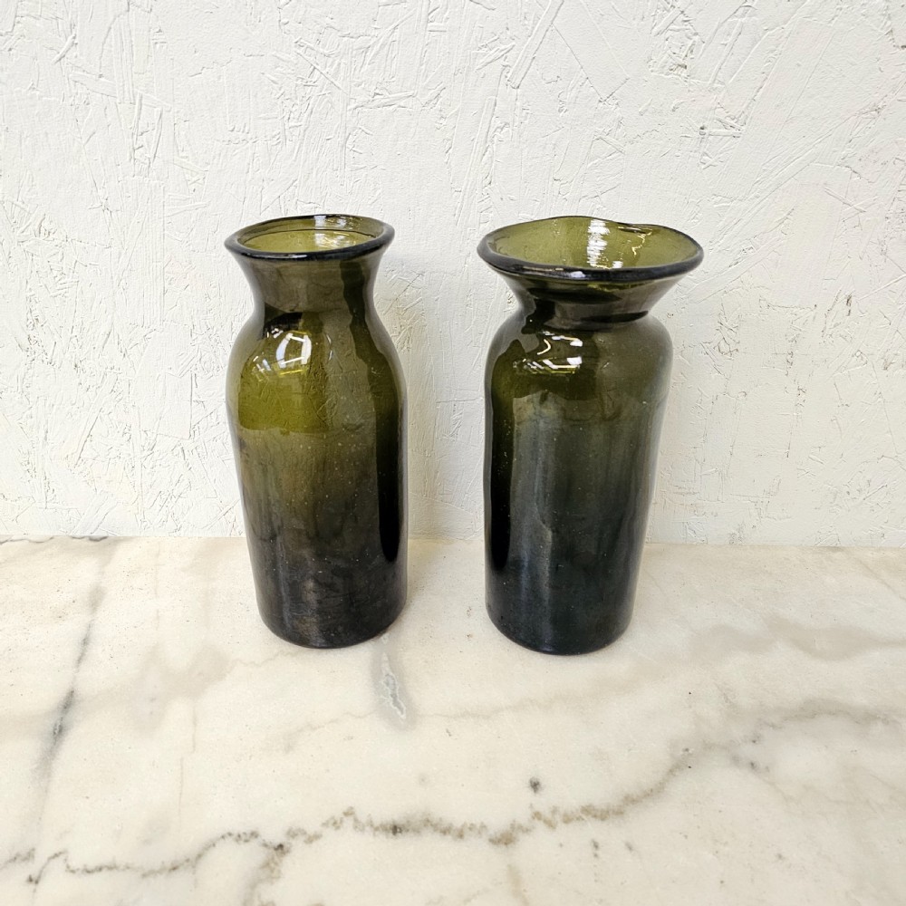 A pair of olive green hand-blown glass jars with cylindrical bases and wide flared rims.
