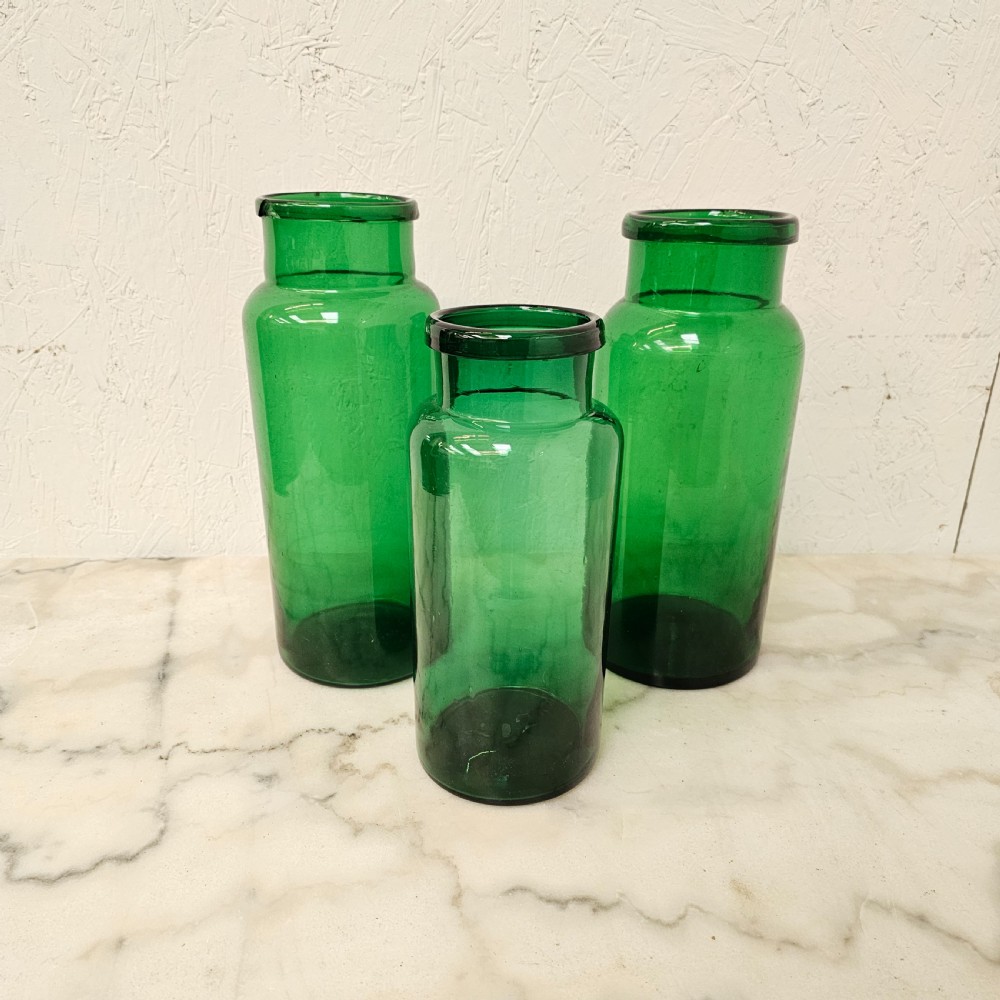 A set of three cylindrical green glass pickling jars of varying heights arranged on a light surface.