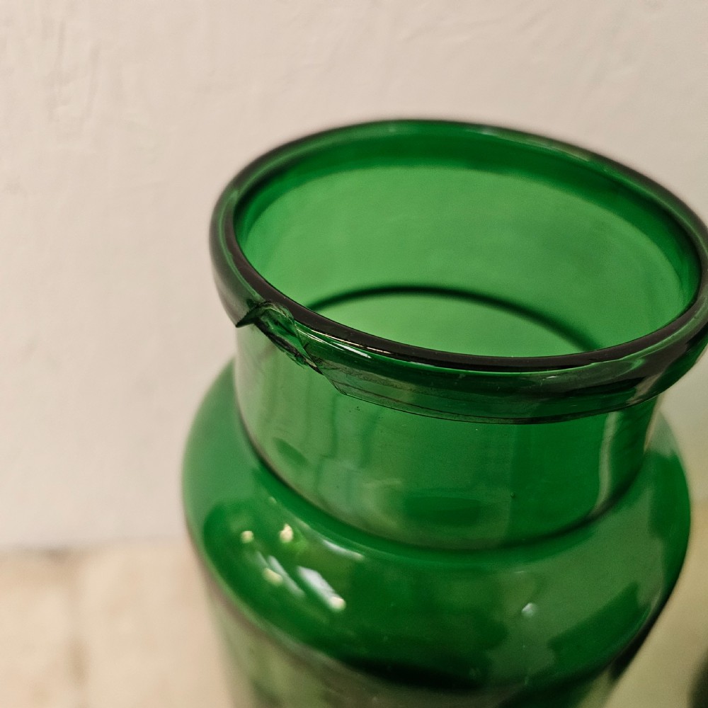 A set of three cylindrical green glass pickling jars of varying heights arranged on a light surface. View IV