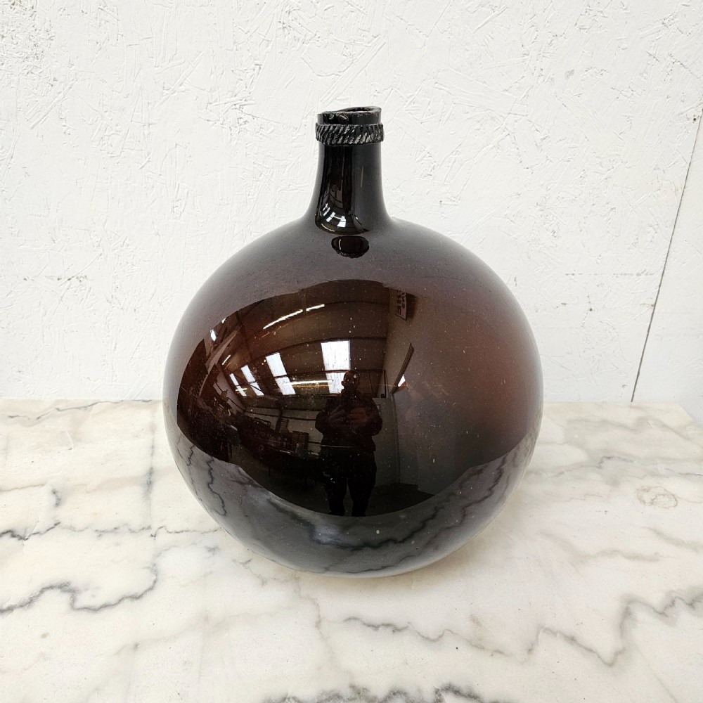 A large globular hand-blown glass jar in deep burgundy with a short tapered neck and an applied string rim.