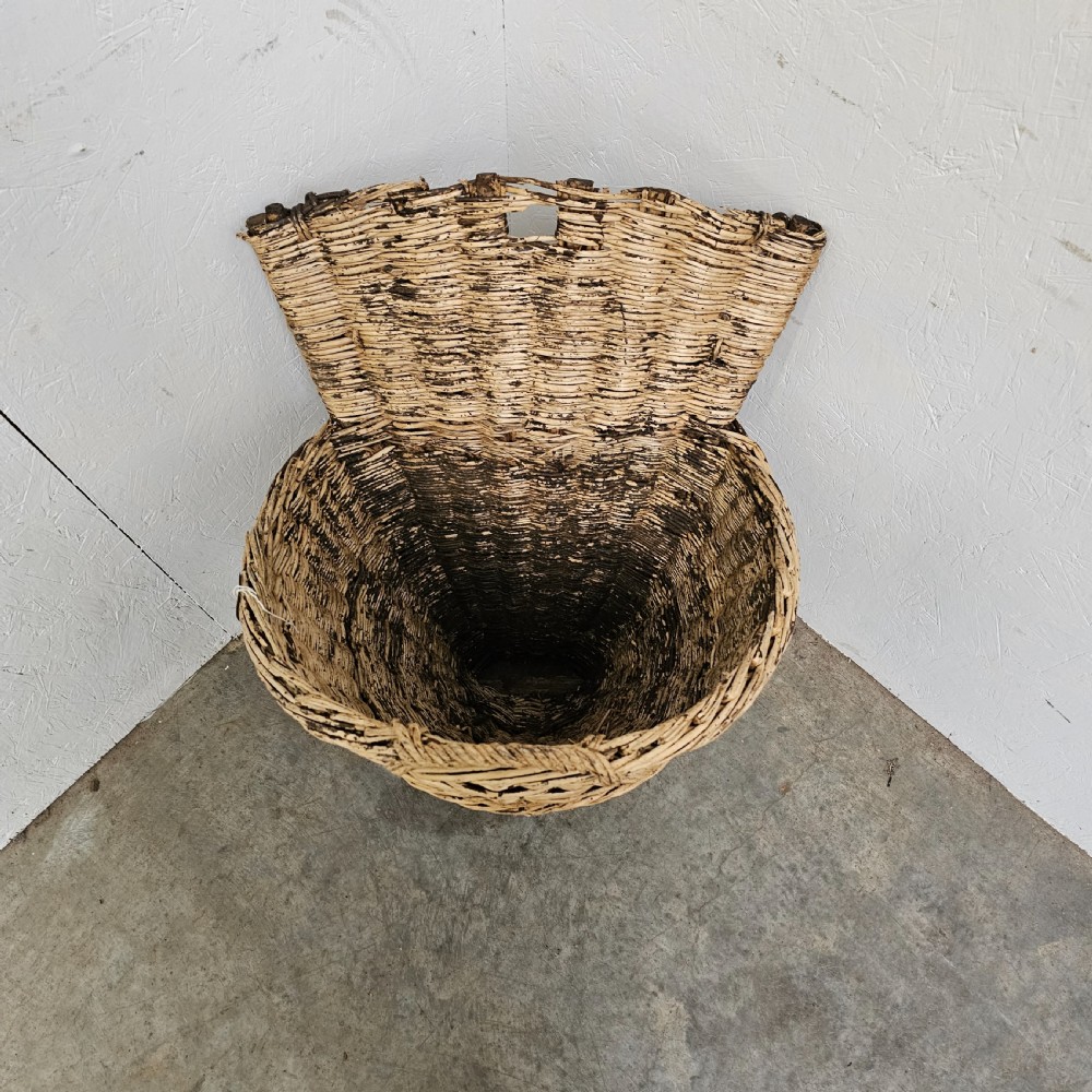A rustic woven wicker grape harvesting hod with a tall flat back extension and an open conical basket body. View II