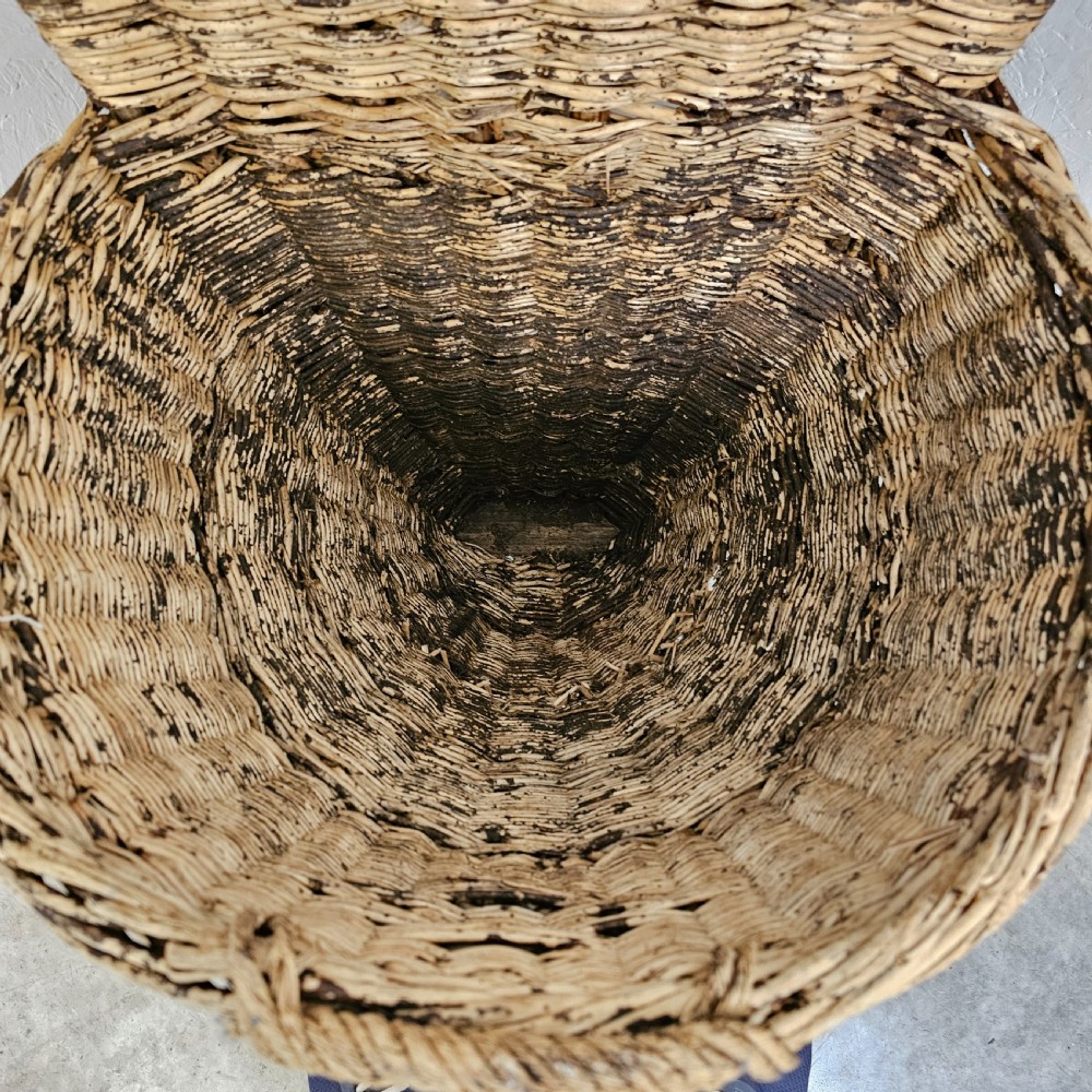 A rustic woven wicker grape harvesting hod with a tall flat back extension and an open conical basket body. View III