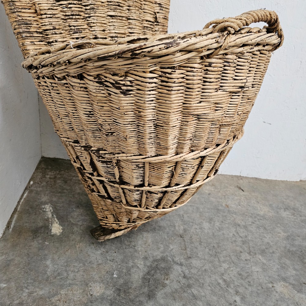 A rustic woven wicker grape harvesting hod with a tall flat back extension and an open conical basket body. View IV