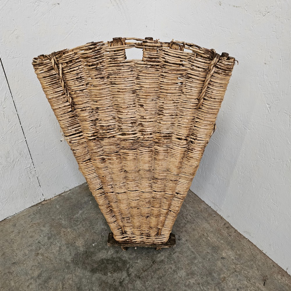 A rustic woven wicker grape harvesting hod with a tall flat back extension and an open conical basket body. View V