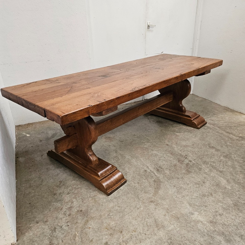 A long French pale oak trestle dining table featuring a solid plank top supported by shaped pedestal legs and a low central stretcher. View II
