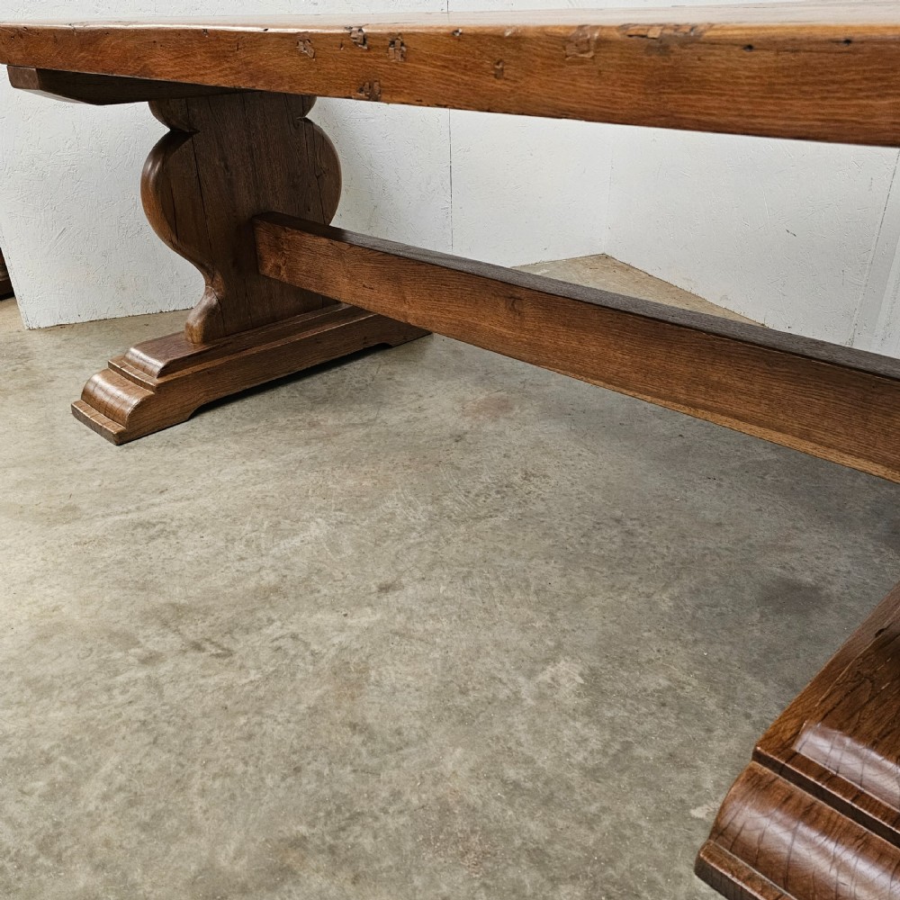 A long French pale oak trestle dining table featuring a solid plank top supported by shaped pedestal legs and a low central stretcher. View III