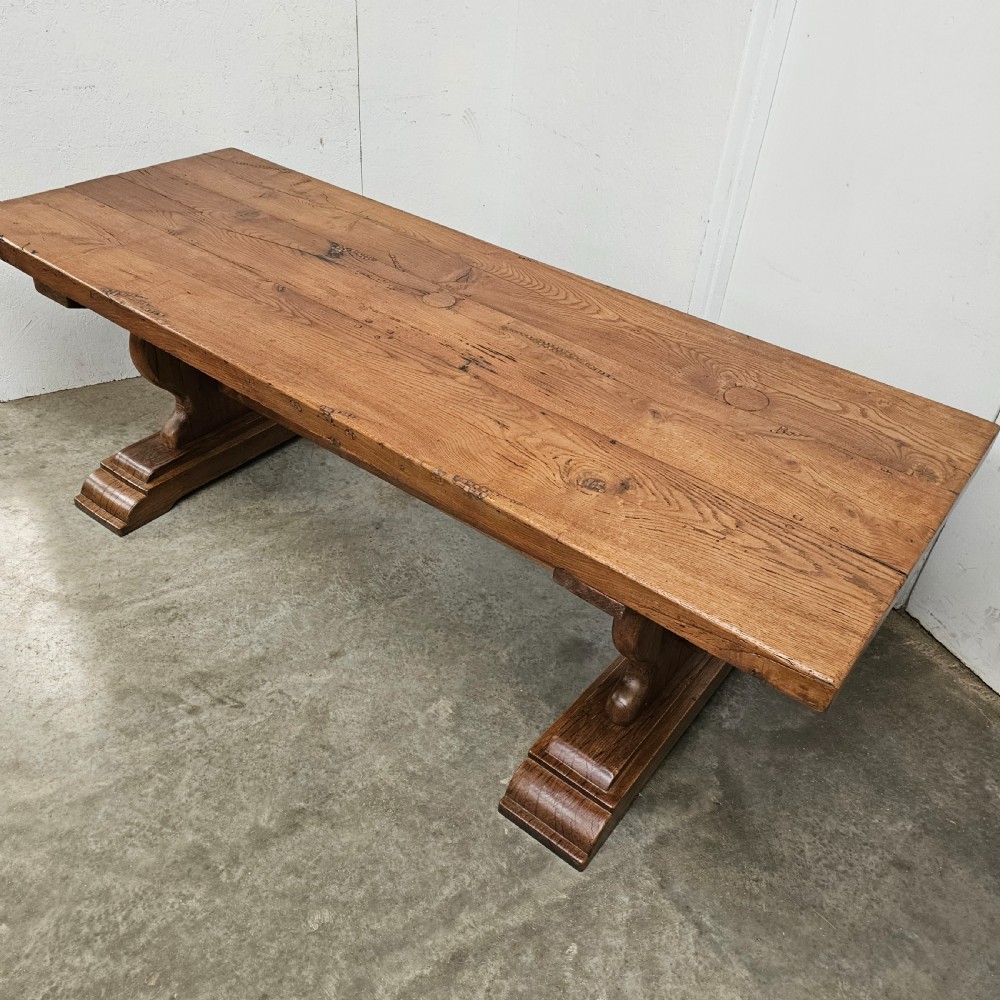 A long French pale oak trestle dining table featuring a solid plank top supported by shaped pedestal legs and a low central stretcher. View V