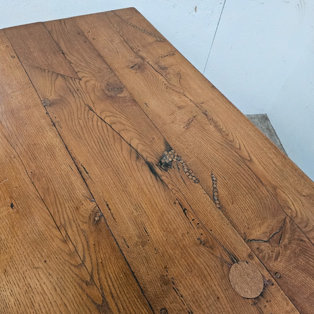A long French pale oak trestle dining table featuring a solid plank top supported by shaped pedestal legs and a low central stretcher. View VII