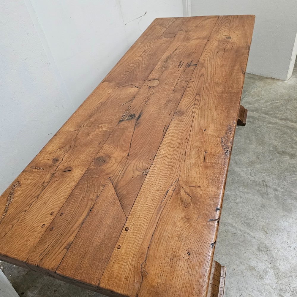 A long French pale oak trestle dining table featuring a solid plank top supported by shaped pedestal legs and a low central stretcher. View VIII