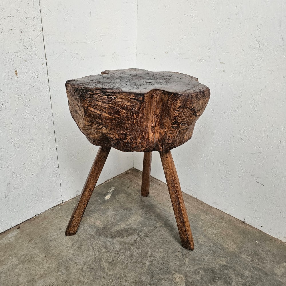 A rustic French oak game block made from a thick tree trunk section set upon three splayed wooden legs.