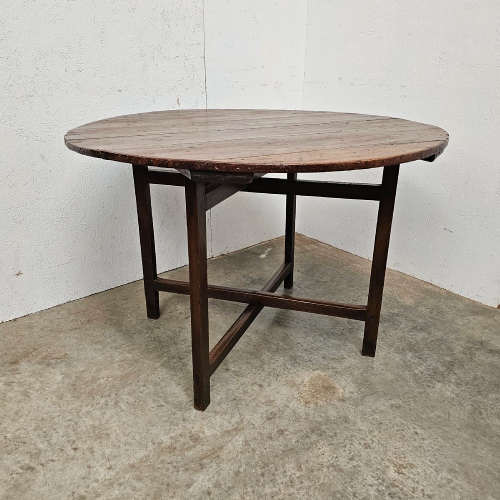 An antique dark oak French folding vineyard table with a circular planked tilt top and a wooden cross-trestle base.