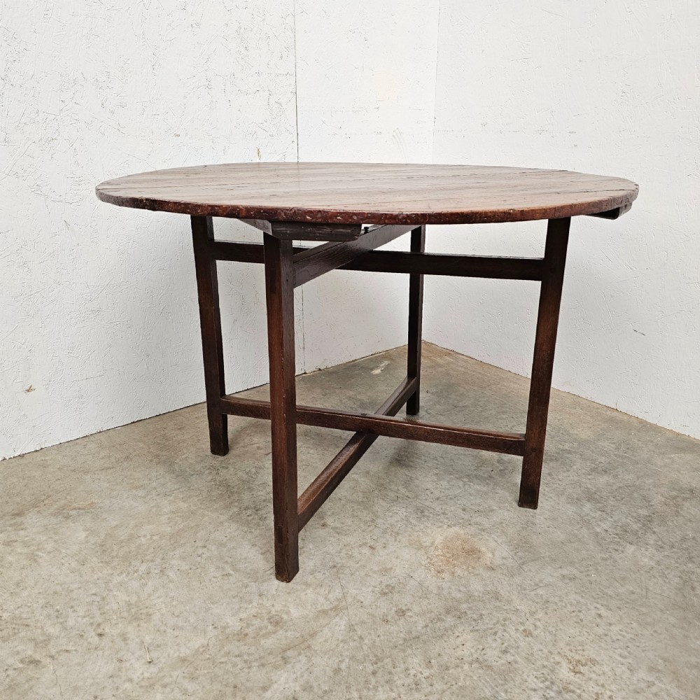 An antique dark oak French folding vineyard table with a circular planked tilt top and a wooden cross-trestle base. View II