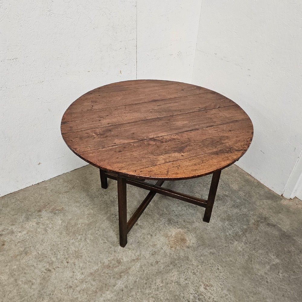 An antique dark oak French folding vineyard table with a circular planked tilt top and a wooden cross-trestle base. View III