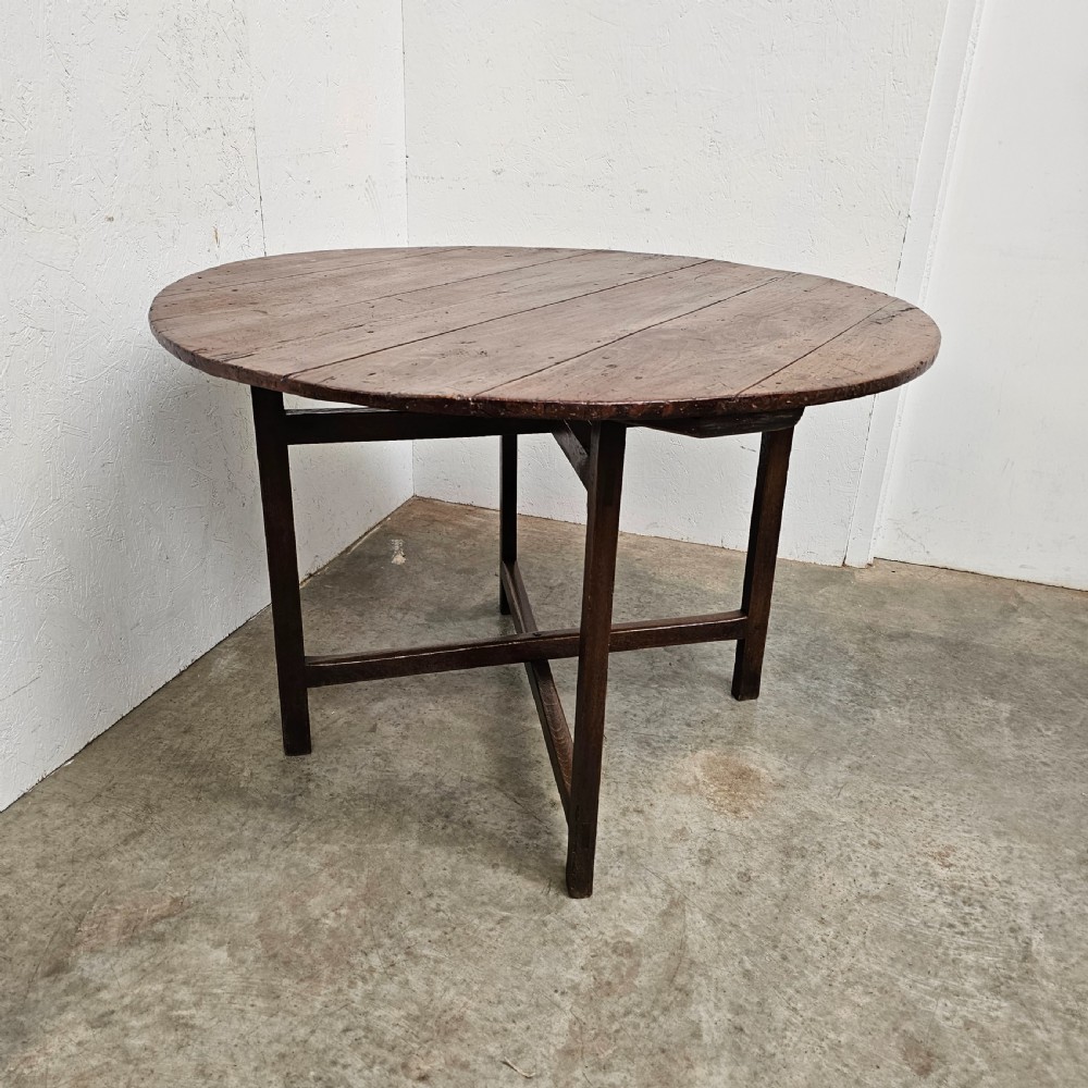 An antique dark oak French folding vineyard table with a circular planked tilt top and a wooden cross-trestle base. View IV