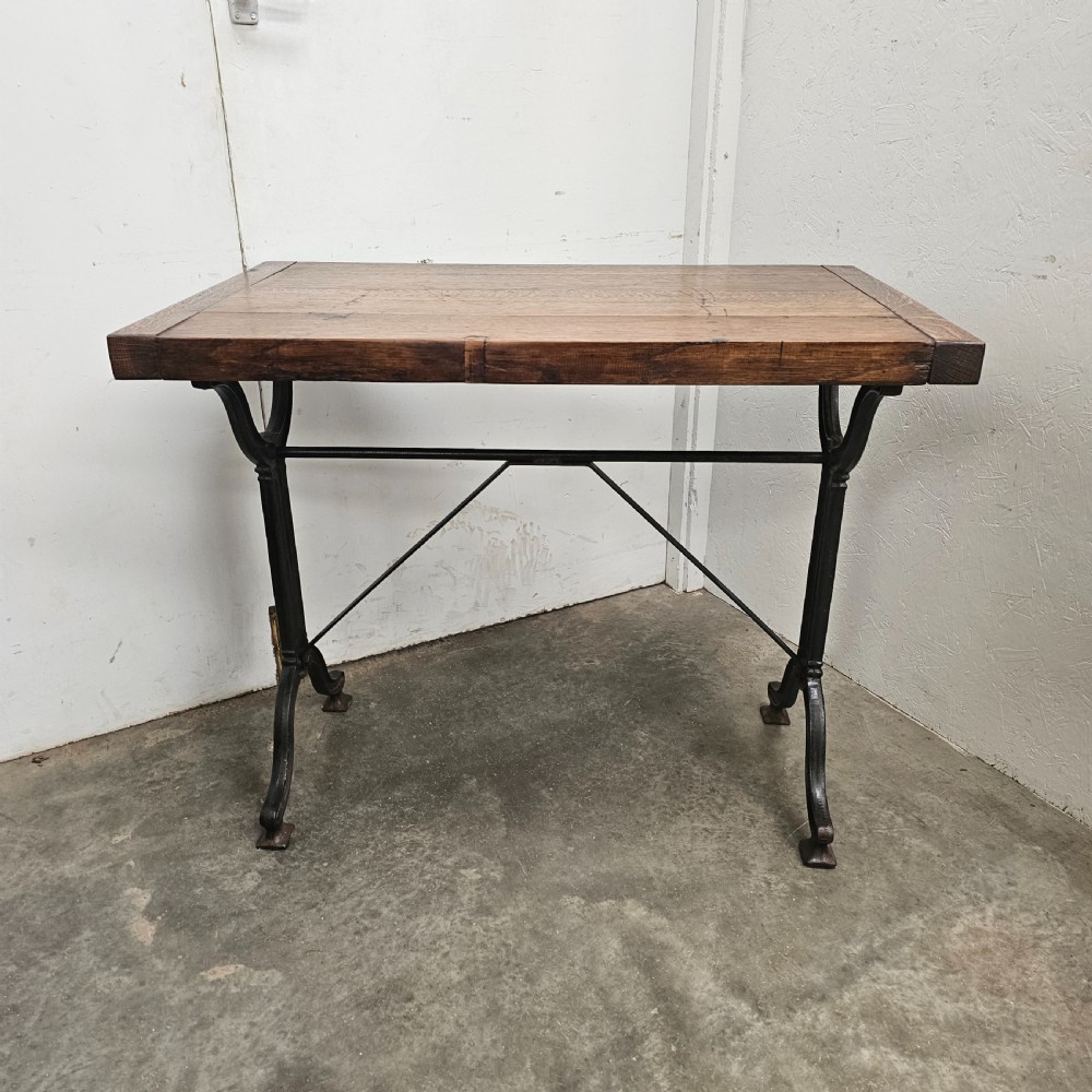 A rectangular oak wood tabletop mounted on a black cast iron frame with cross-braced legs.