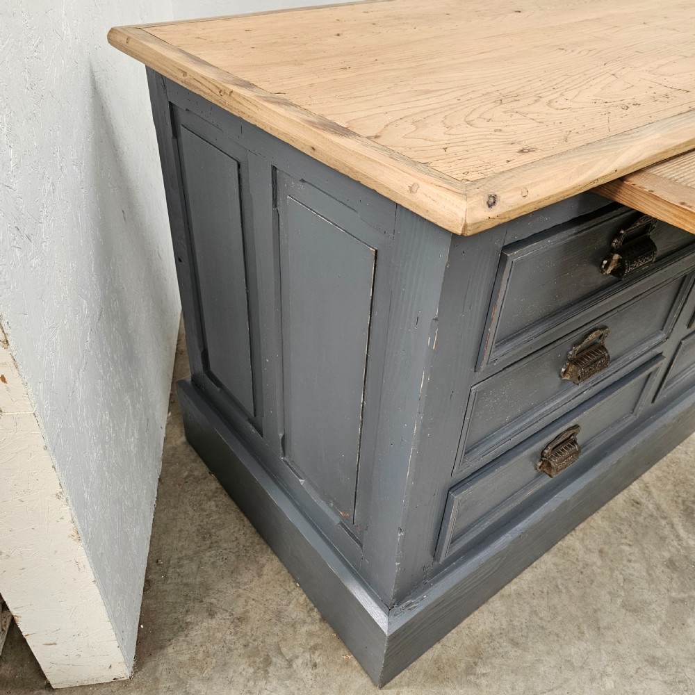 A long French shop counter featuring twelve drawers painted in dark grey with metal cup handles and a natural scrubbed pine top surface. View IX