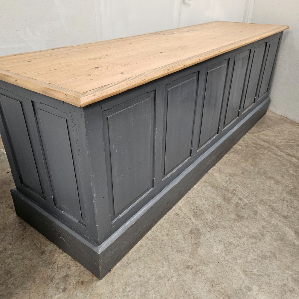 A long French shop counter featuring twelve drawers painted in dark grey with metal cup handles and a natural scrubbed pine top surface. View X