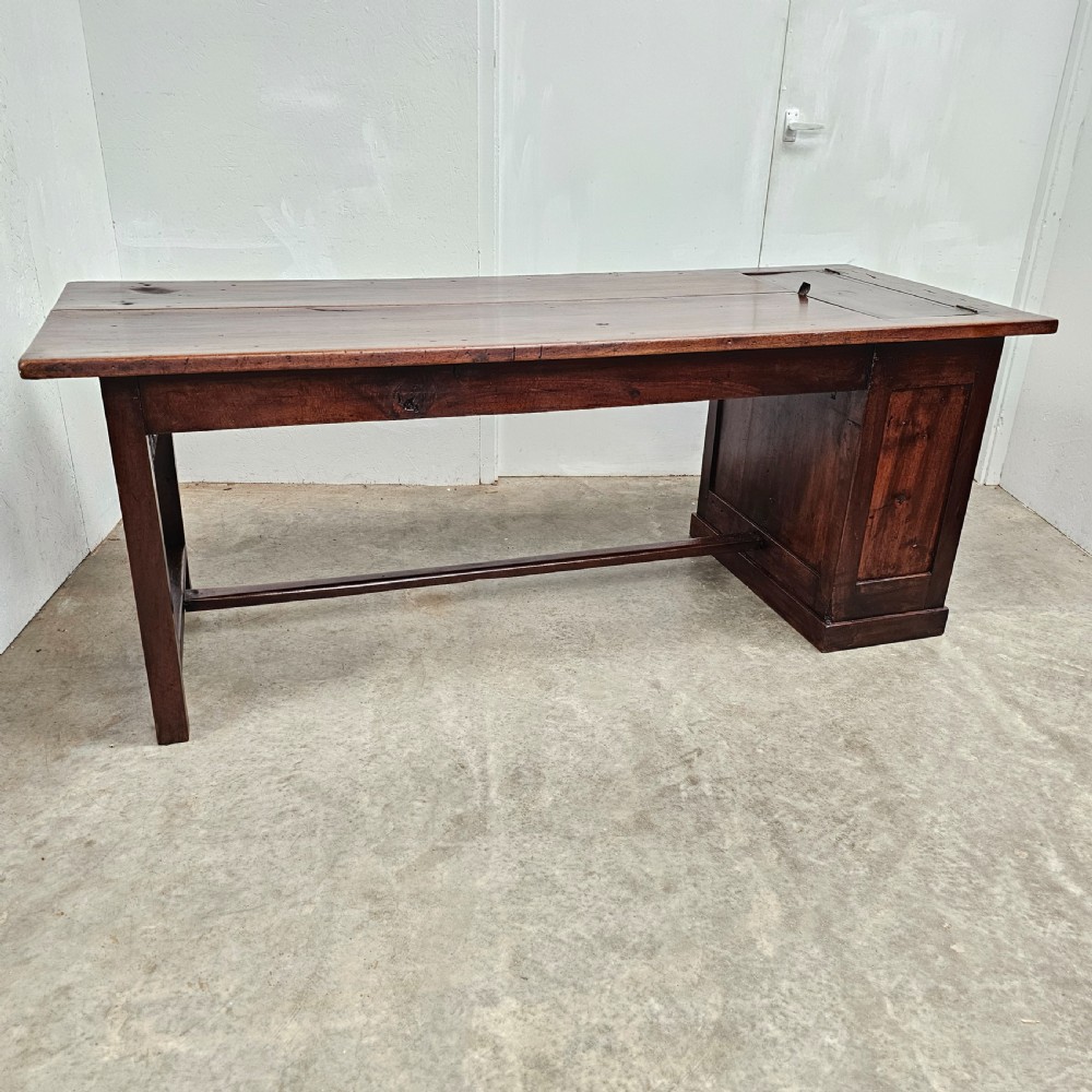 An antique French dark walnut bread prep table featuring a two-board top, side pedestal storage compartment, and lower stretcher base.