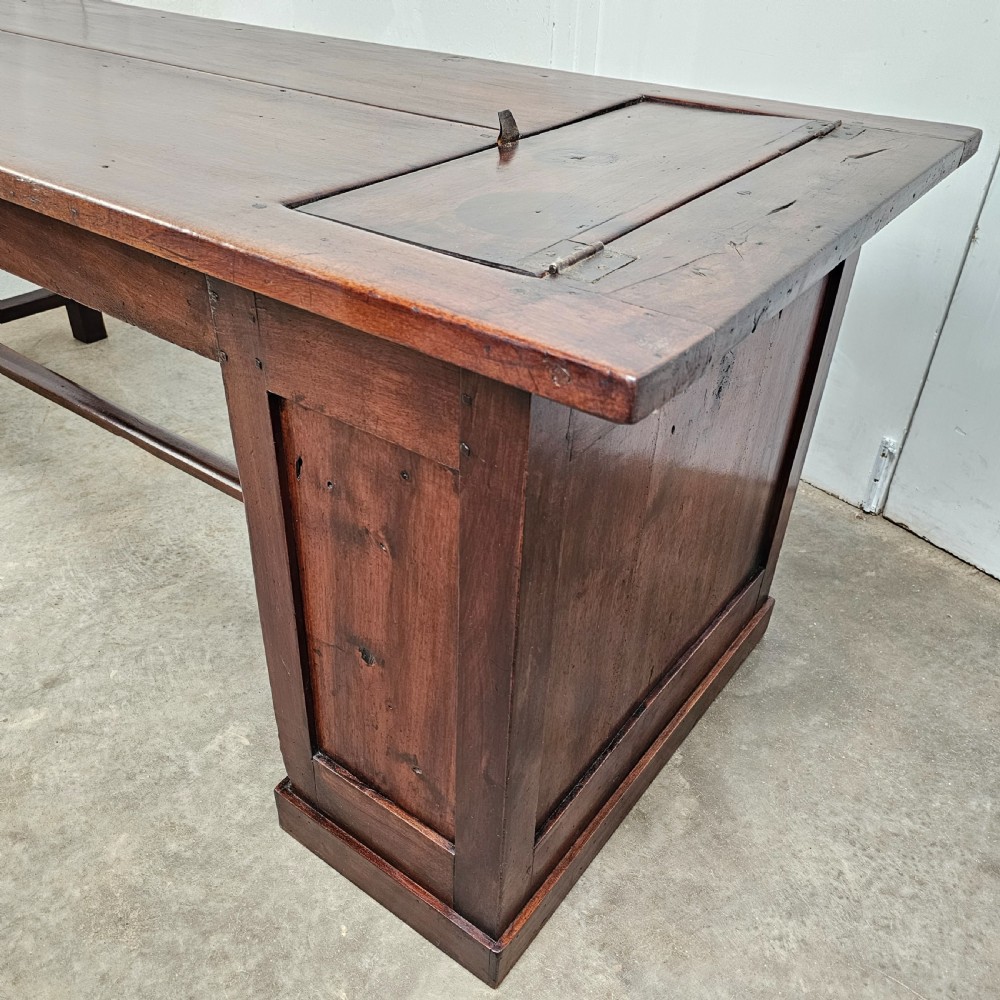 An antique French dark walnut bread prep table featuring a two-board top, side pedestal storage compartment, and lower stretcher base. View VI