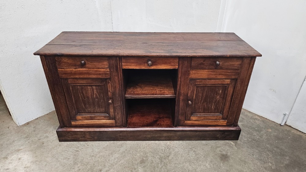A 19th-century French dark chestnut dresser base featuring three top drawers above two panelled cupboard doors and a central open shelving section, set on a solid plinth base.