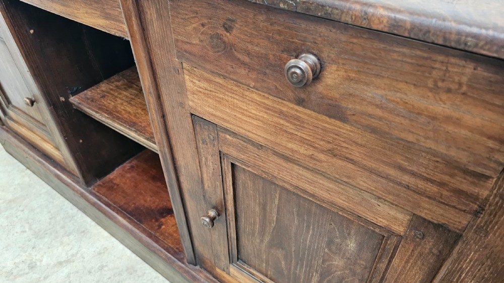 A 19th-century French dark chestnut dresser base featuring three top drawers above two panelled cupboard doors and a central open shelving section, set on a solid plinth base. View VI