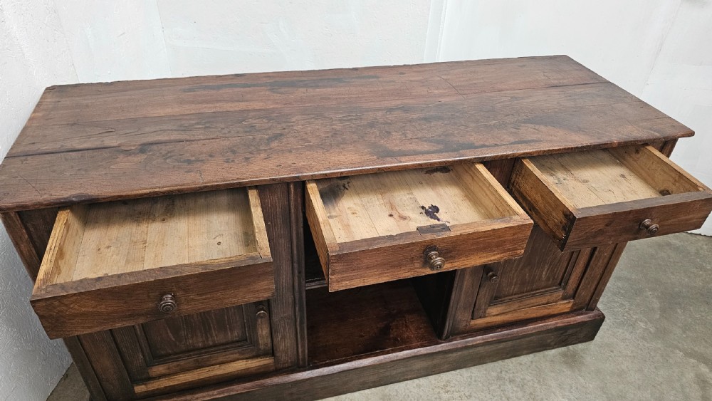 A 19th-century French dark chestnut dresser base featuring three top drawers above two panelled cupboard doors and a central open shelving section, set on a solid plinth base. View VIII