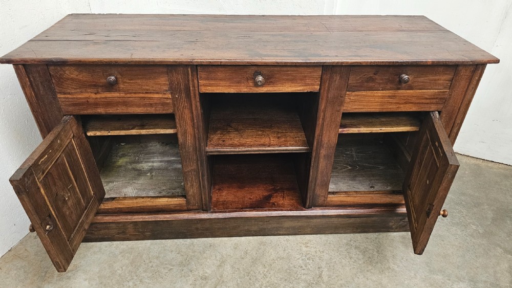 A 19th-century French dark chestnut dresser base featuring three top drawers above two panelled cupboard doors and a central open shelving section, set on a solid plinth base. View IX