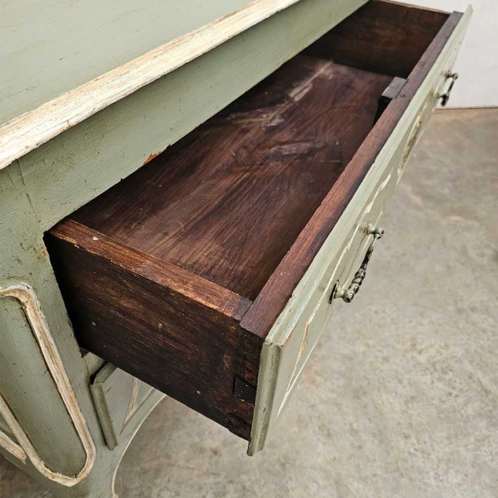 An 18th-century French provincial painted commode featuring two long drawers finished in muted green paint with cream trim and metal handles. View V