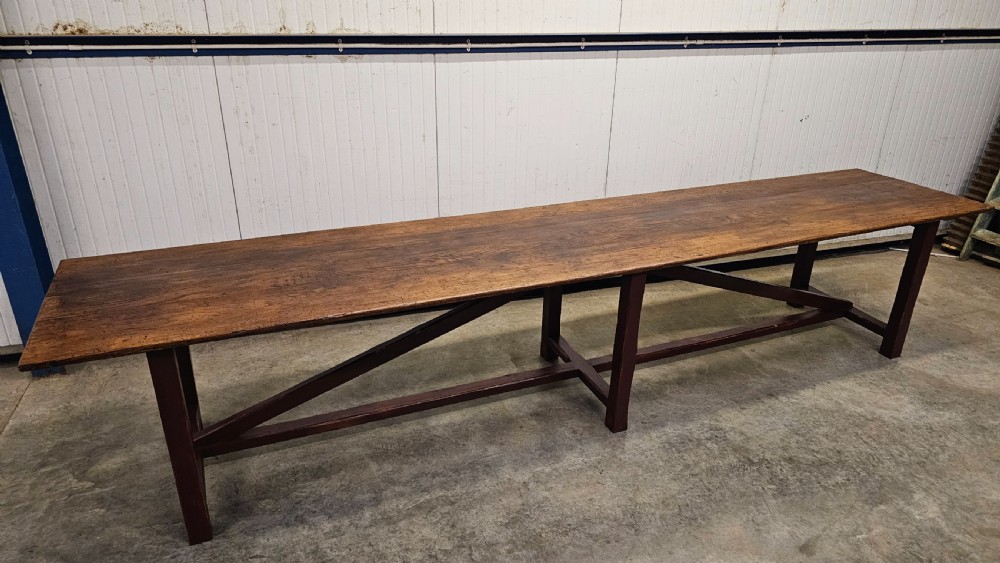 An exceptionally long antique pine harvest table featuring a plank wood top supported by a dark stained frame with cross-bracing. View II