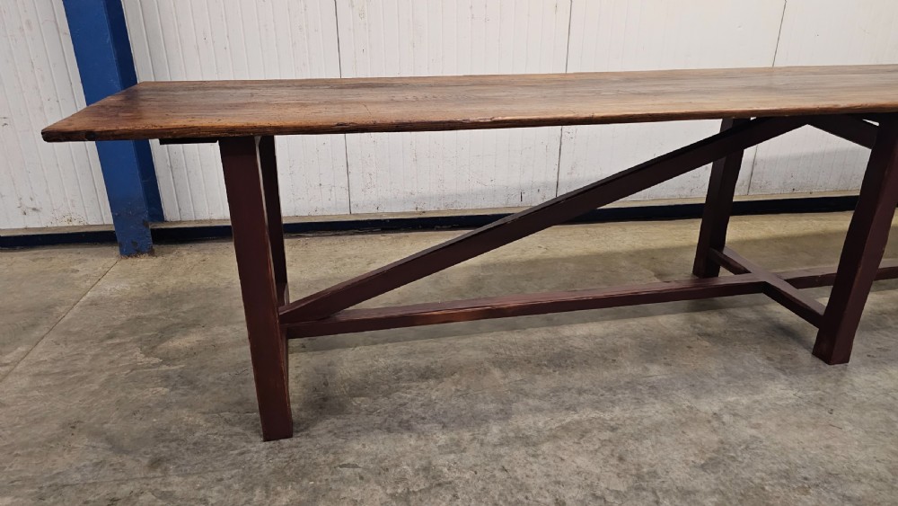 An exceptionally long antique pine harvest table featuring a plank wood top supported by a dark stained frame with cross-bracing. View III