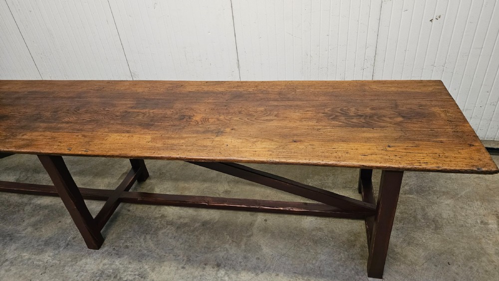 An exceptionally long antique pine harvest table featuring a plank wood top supported by a dark stained frame with cross-bracing. View IV