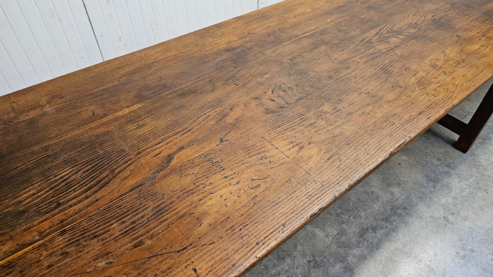 An exceptionally long antique pine harvest table featuring a plank wood top supported by a dark stained frame with cross-bracing. View VII