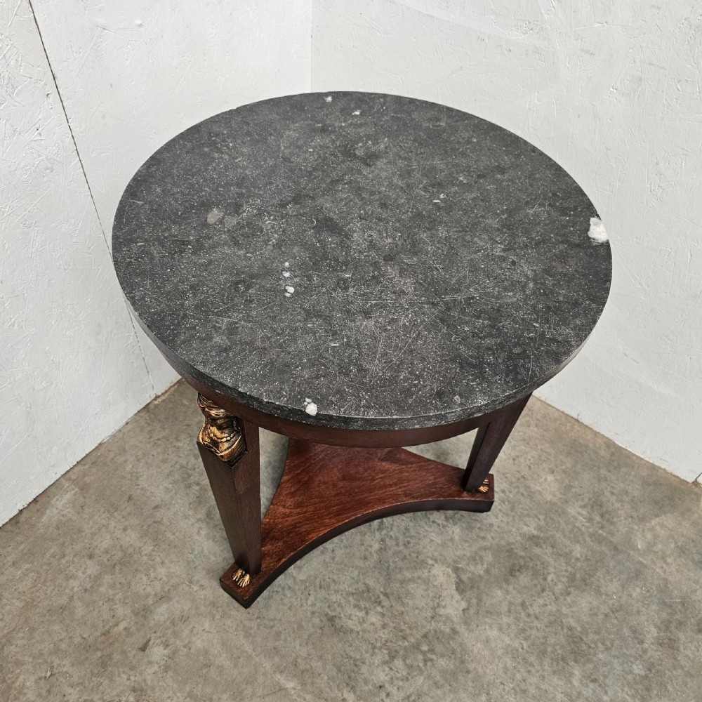A circular 19th-century French Empire style gueridon featuring a dark marble top supported by tapered mahogany legs adorned with gilt female busts and a triform base. View II