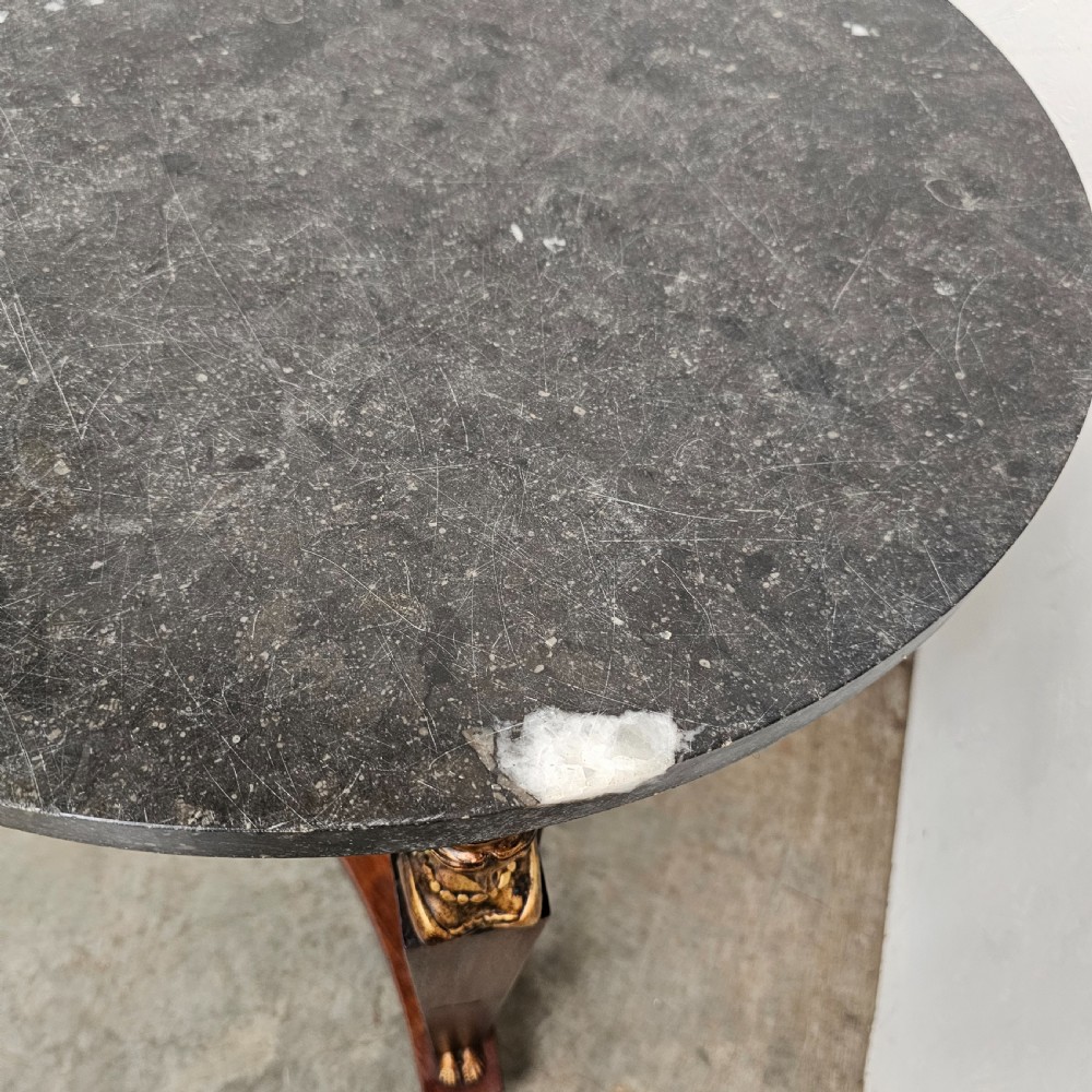 A circular 19th-century French Empire style gueridon featuring a dark marble top supported by tapered mahogany legs adorned with gilt female busts and a triform base. View IV