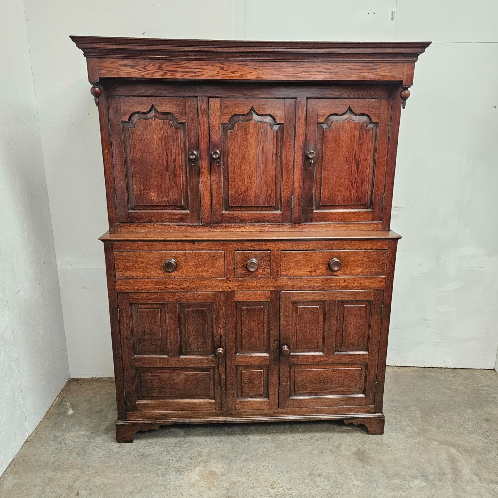 An eighteenth-century dark oak Welsh deuddarn press cupboard featuring three ogee arched upper doors above drawers and fielded lower panel doors.