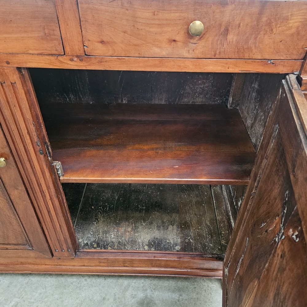 A tall cherrywood Directoire buffet featuring three drawers above two large panelled cupboard doors with brass knobs and fluted pilasters. View V