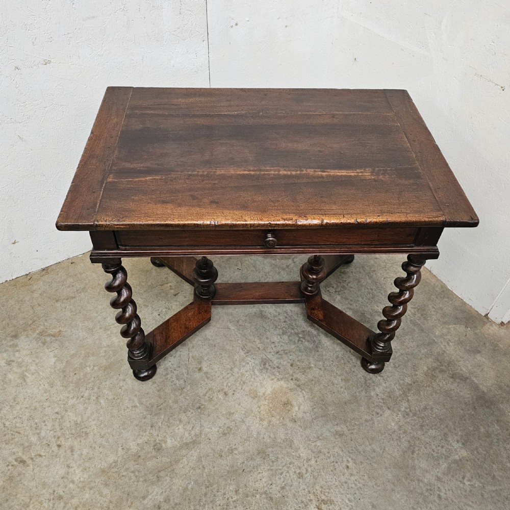 An antique dark walnut table featuring four barley twist legs, a stretcher base with decorative finials, and a single drawer with a central round wooden knob. View II