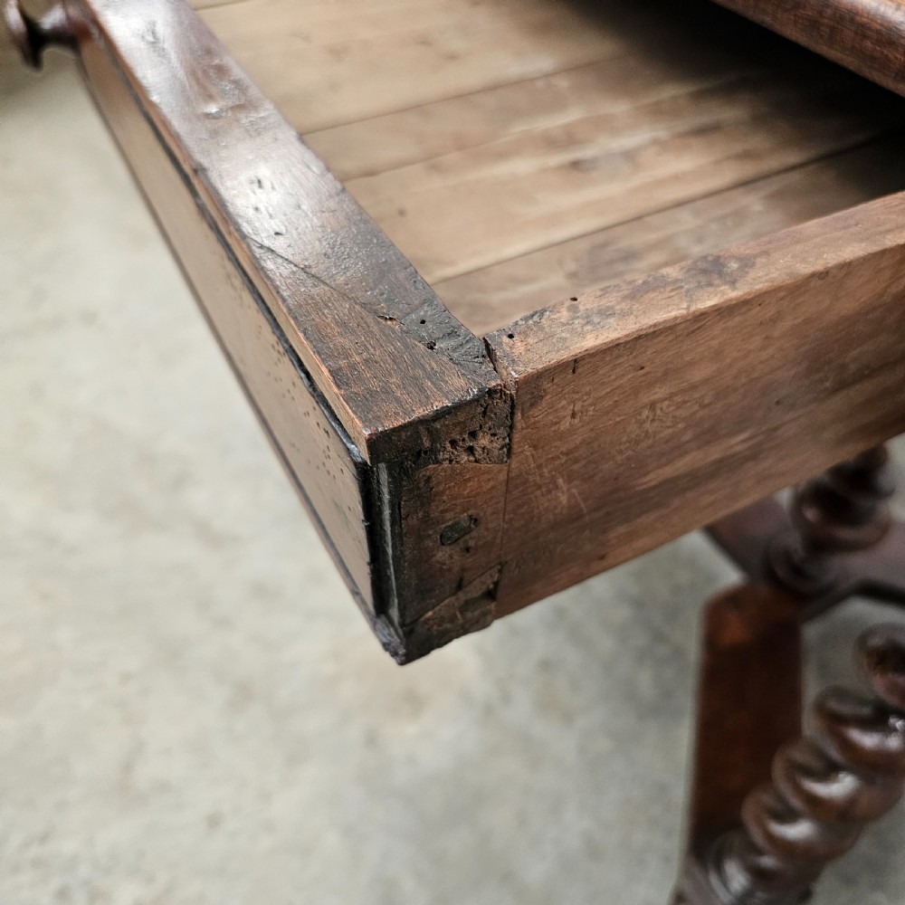 An antique dark walnut table featuring four barley twist legs, a stretcher base with decorative finials, and a single drawer with a central round wooden knob. View VI