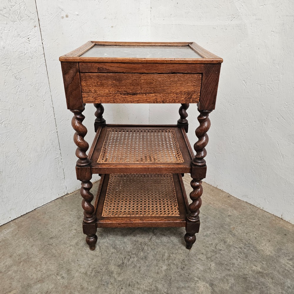 A French oak tiered etagere featuring an inset marble top, two woven cane lower shelves, and turned barley-twist supports.